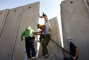 Palestinian demonstrators climb on a panel of the controversial Israeli barrier after it was breached during a protest in the West Bank village of Nilin